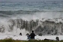 A woman sits by the shore while looking at waves breaking as Typhoon Koinu approaches, in Taitung, Taiwan, Oct 4, 2023. 