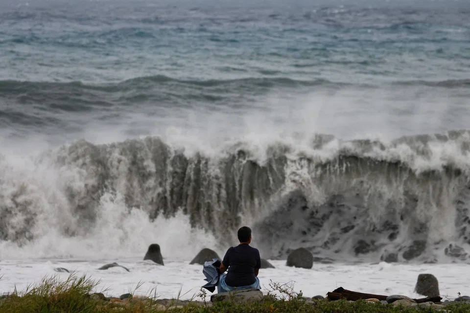 A woman sits by the shore while looking at waves breaking as Typhoon Koinu approaches, in Taitung, Taiwan, Oct 4, 2023. 