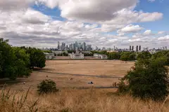 A large area of parched grass in Greenwich Park in front of a view of skyscrapers in the Canary Wharf financial, business and shopping district in the Greenwich district of London, Aug 3, 2022.
