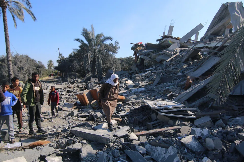Palestinians walk across the rubble of a collapsed building following an Israeli airstrike in the Zuwayida district of central Gaza, Feb 22, 2024. 