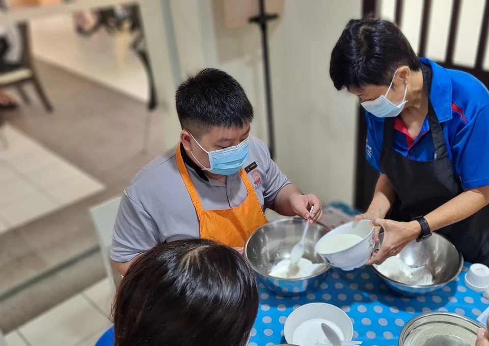 Singapore Pools staff volunteer preparing batter for the cupcakes with the student from Metta School