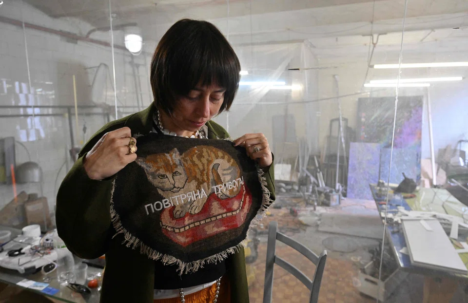 Ukrainian artist Zhanna Kadyrova shows her creation with signing "Air raid alert" in her workshop in Kyiv; a Kyiv gallery is currently displaying her “Anxiety” series – tapestries depicting kitsch flowers and cats, which she over-embroiders with air raid warnings. 