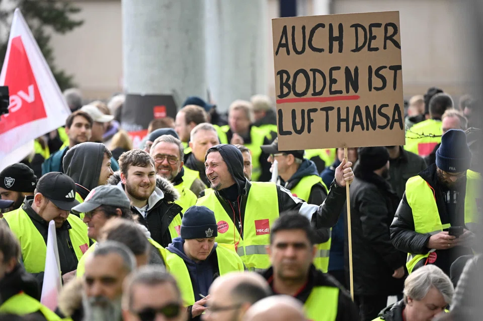 Lufthansa employees protest with a placard reading 'Also the ground is Lufthansa' outside Frankfurt Airport, Frankfurt, Germany on Feb 20, 2024.