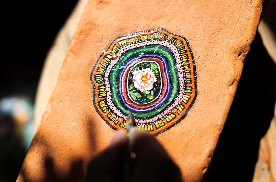 Ben Wilson, shows his painting on a piece of chewing gum, stuck on a brick, in his home studio in Muswell Hill, London.