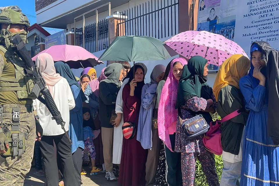 A soldier stands guard as voters wait in line outside a polling station during the nationwide village and youth representative elections in Marawi, Mindanao island, Philippines on Oct 30, 2023. 