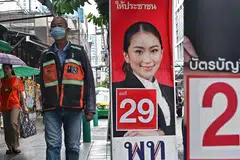 People walk past a campaign poster for Pheu Thai candidate Paetongtarn Shinawatra along a street in Bangkok on May 10, 2023.