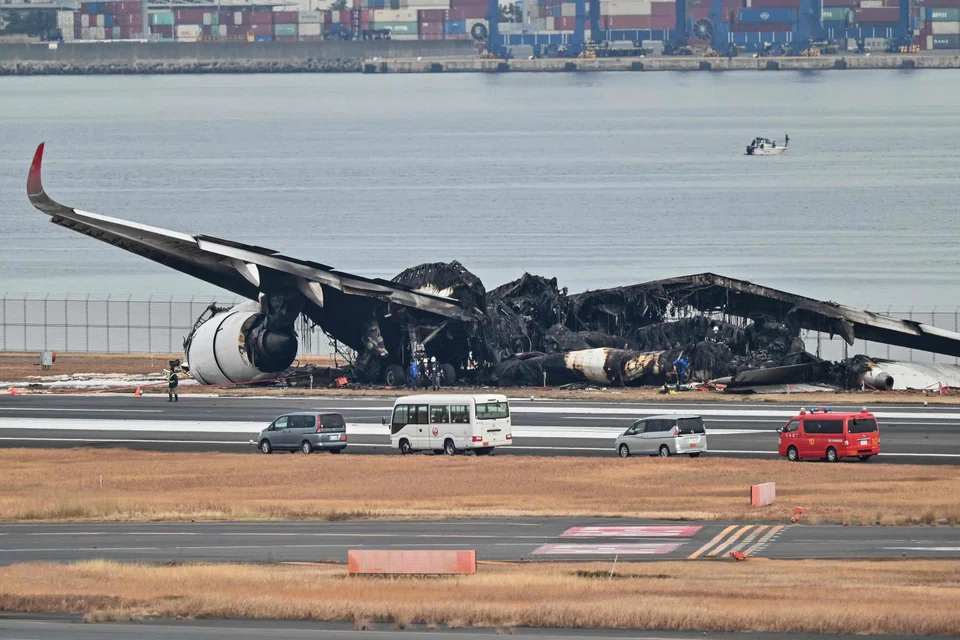 Officials look at the burnt wreckage of a Japan Airlines passenger plane on the tarmac at Tokyo International Airport at Haneda, Tokyo on Jan 3, 2024, the morning after the JAL airliner hit a smaller coast guard plane on the ground. 