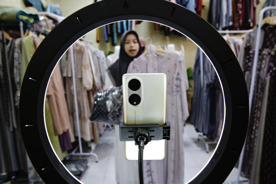 A sales promoter holds a dress as she live-streams on an e-commerce platform at a shop in Depok, Indonesia.