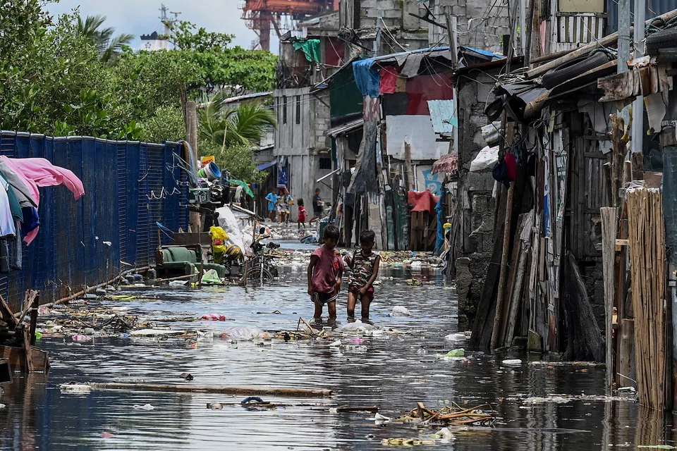Children walk through a flooded area due to high tide in Baseco, one of the biggest slums in Manila on Aug 15, 2022. The Vulnerable Group of Twenty (V20) – a group of 55 economies exposed to the fallout from climate change – expect debt service payments to rise to US$69 billion by 2024.