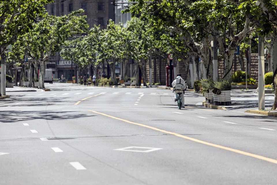 A worker in personal protective equipment (PPE) rides a bicycle along a nearly-empty road in Shanghai on May 5, 2022. 