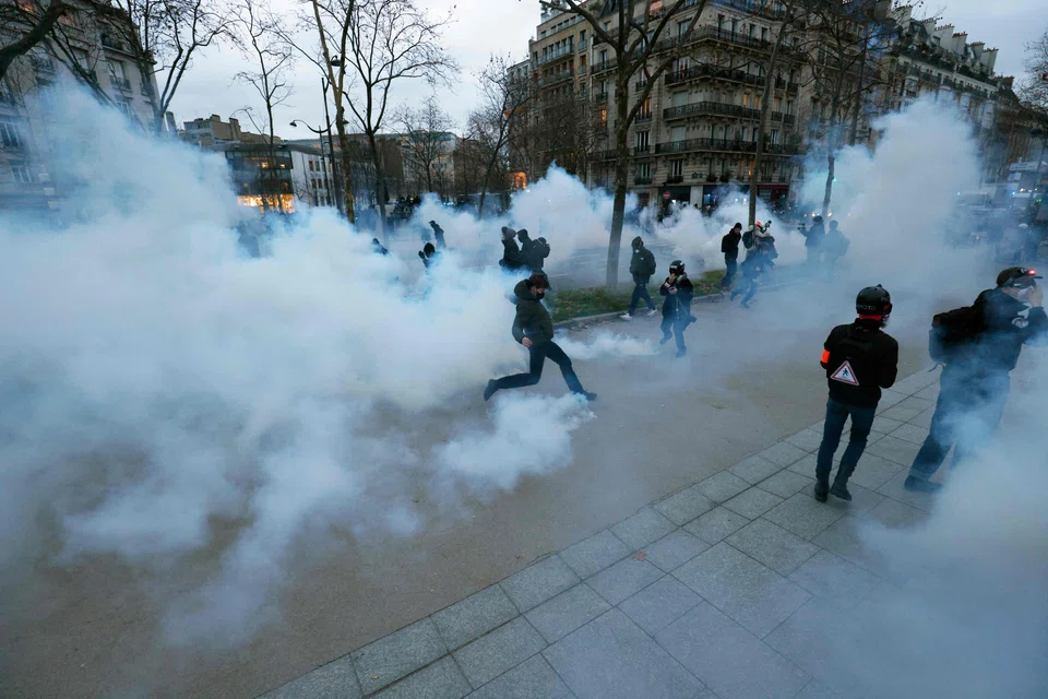 A protester (centre) tries to kick a fuming tear gas pellet during a demonstration on a second day of nationwide strikes and protests, in Paris on Jan 31, 2023. 