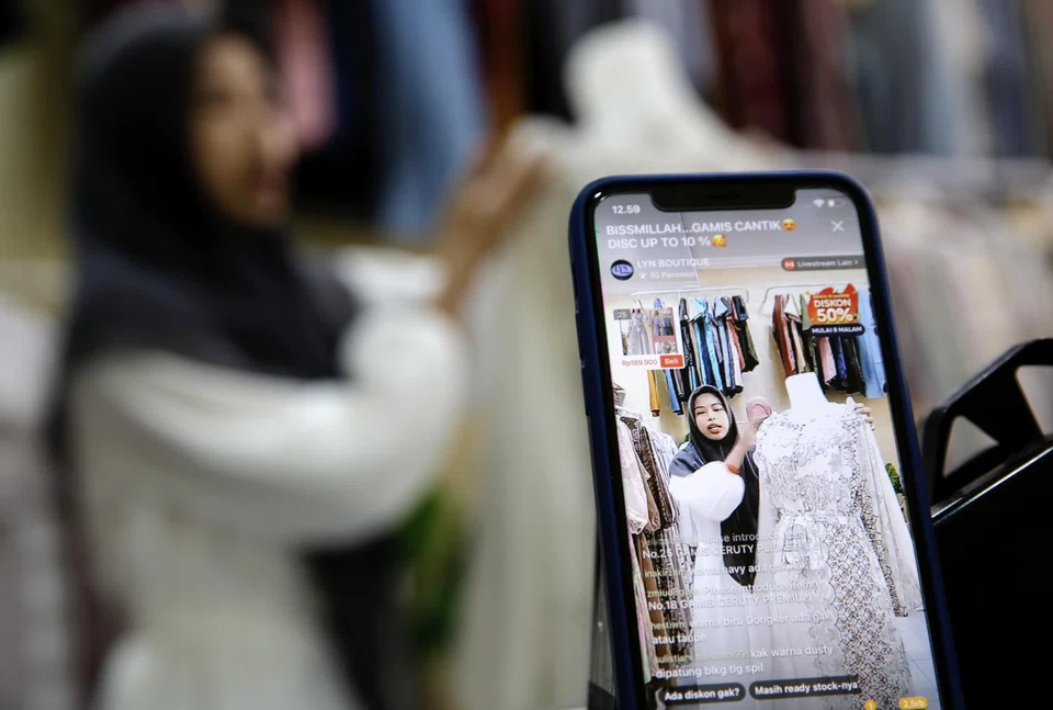 A sales promoter showcasing a dress as she livestreams on an e-commerce platform at a shop in Depok, Indonesia.