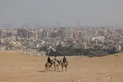 The city skyline of Cairo beyond horse riders on the Giza pyramid complex in Giza, Egypt. Leaders around the world will gather in Sharm el-Sheikh for the annual UN Climate Change conference, known this year as COP27.