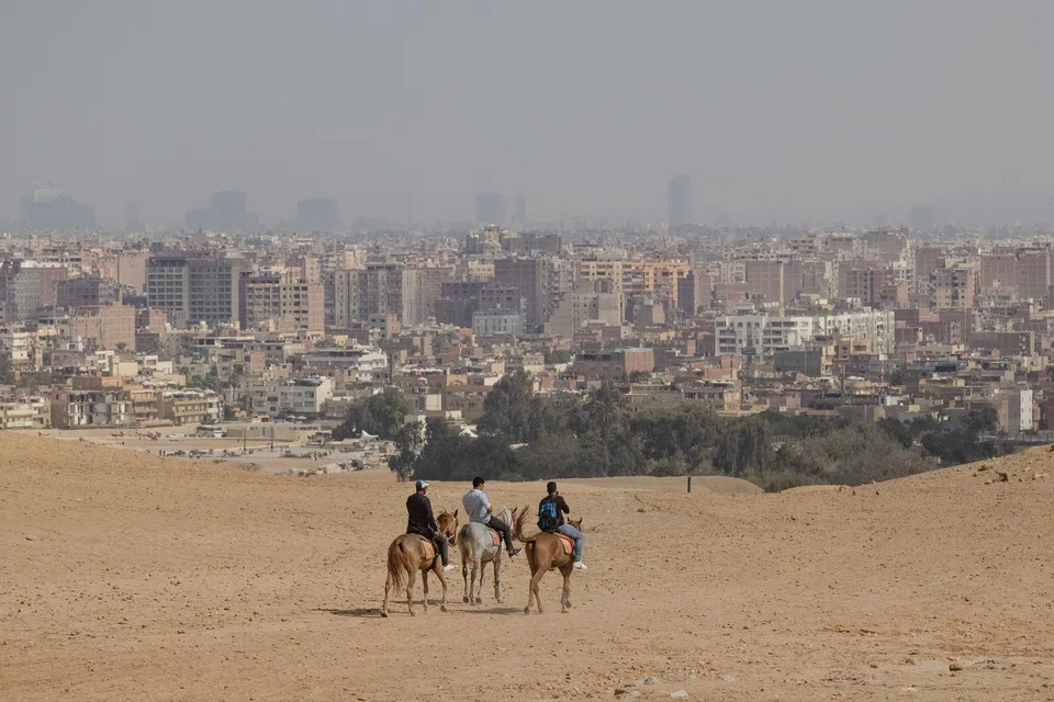 The city skyline of Cairo beyond horse riders on the Giza pyramid complex in Giza, Egypt. Leaders around the world will gather in Sharm el-Sheikh for the annual UN Climate Change conference, known this year as COP27.