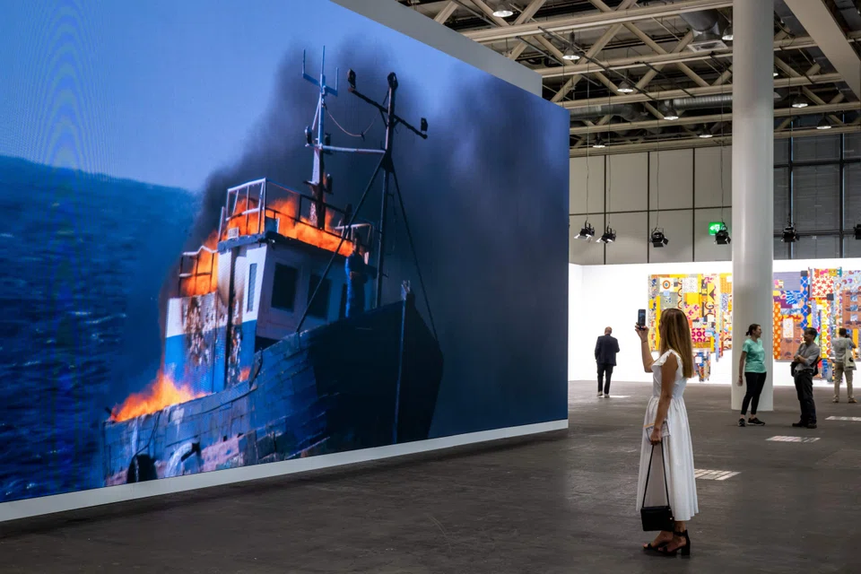 A visitor takes a picture of 'Jam Proximus Ardet, the last video' (2021) by Algerian-French contemporary artist Adel Abdessemed, displayed at the Art Basel fair.