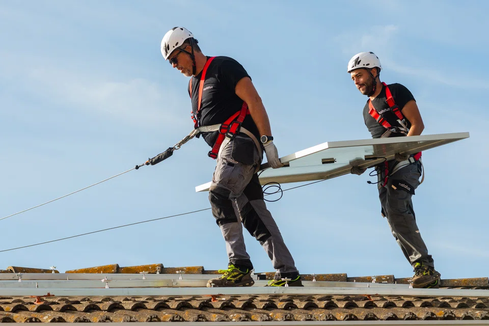 Engineers from Holaluz-Clidom carry a solar panel across the roof during a residential installation in Madrid, Spain. Solar energy installations on rooftops have been surging in Spain, which aims to produce 67 per cent of its electricity from renewables by 2026. Foreign power companies are investing in the country to build the infrastructure to reach that goal.  