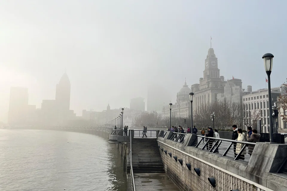 People stand on the Bund as buildings along the Huangpu river are seen shrouded in fog, amid a red alert for heavy fog in Shanghai, China, Dec 29, 2023. 