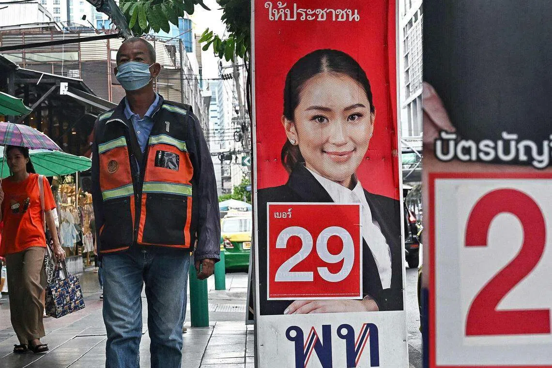 People walk past a campaign poster for Pheu Thai candidate Paetongtarn Shinawatra along a street in Bangkok on May 10, 2023.