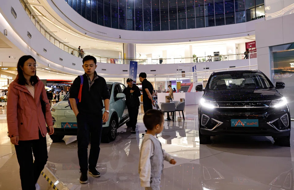 People walk past a Dayun Auto's electric vehicles booth at a shopping mall in Beijing, China, Nov 3, 2023. 