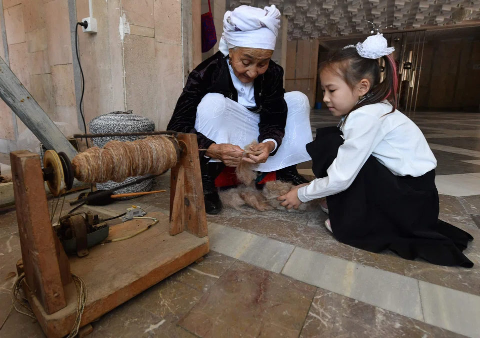 Tashkan Khakimova teaching a young girl the art of weaving a shyrdak, a traditional Kyrgyz woollen rug.