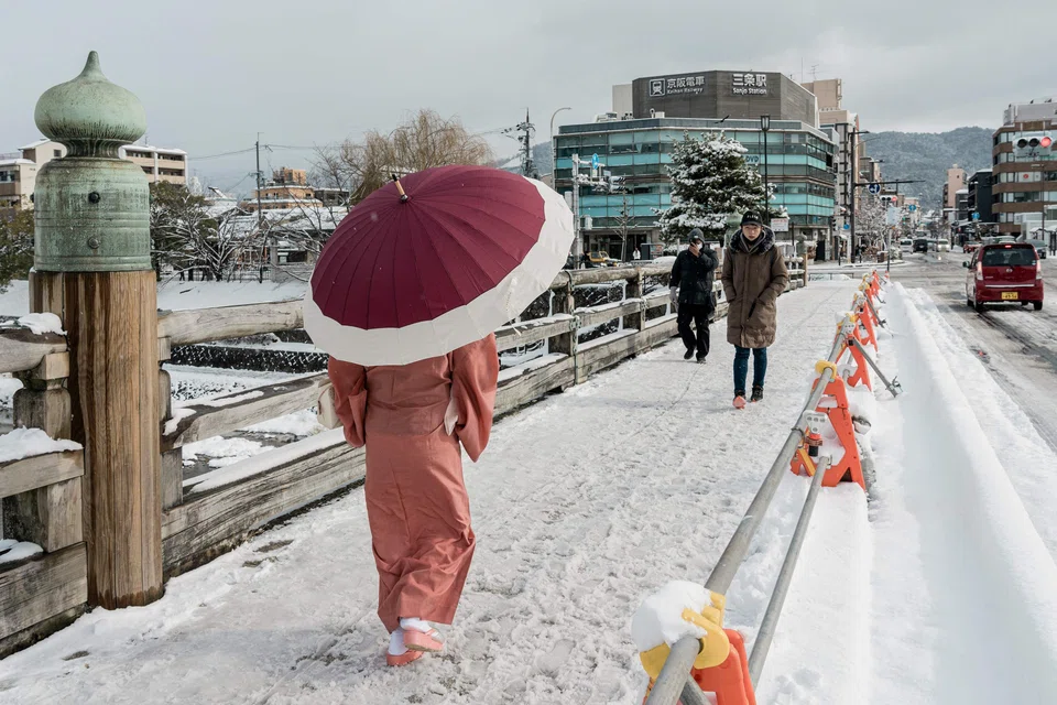 Pedestrians cross a snow-covered bridge over the Kamo River in Kyoto on Jan 25, 2023, after heavy snow and strong winds overnight affected wide areas of the country. 