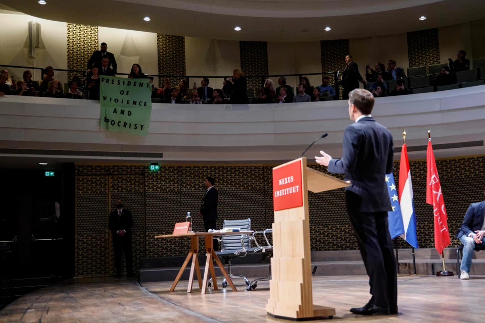Students deploy a protest banner which reads "President of violence and hypocrisy" during French President Emmanuel Macron's speech to the Nexus Institute in The Hague on April 11, 2023 as part of a state visit to the Netherlands. 