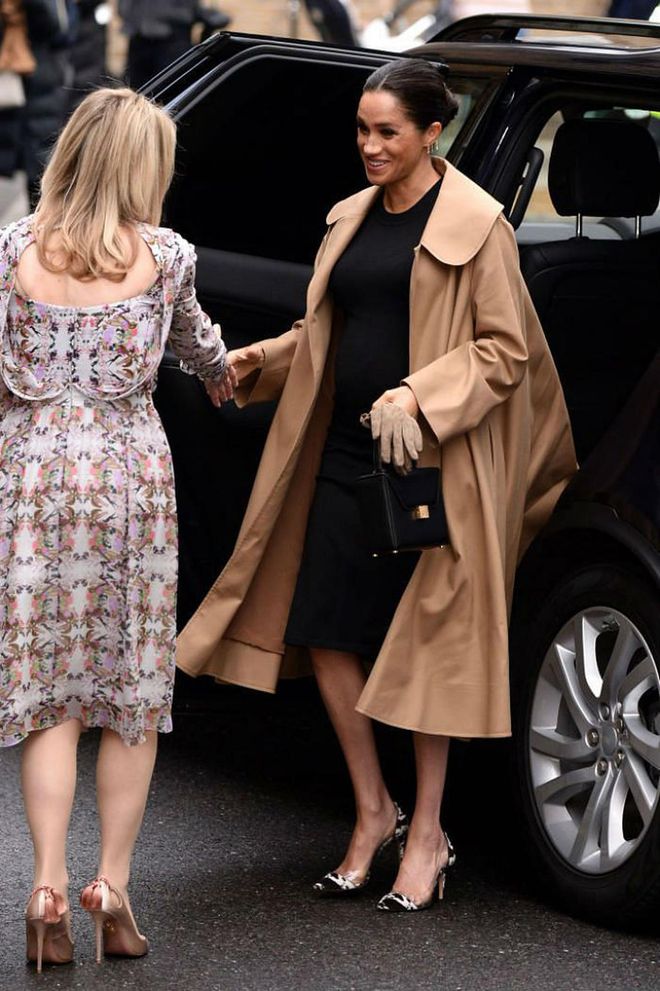 Meghan Markle wore a beautiful camel coat by Oscar de la Renta over a black dress by maternity brand Hatch for her first official engagement as the royal patron of women's charity Smart Works. She paired her look with Kimai earrings and Gianvito Rossi cow-print pumps.