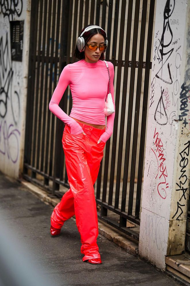 MILAN, ITALY - FEBRUARY 24: Alexandra Guerain wears silver headphones, a pale pink long sleeves t-shirt, a white shiny leather shoulder bag, orange sunglasses, red neon shiny leather large pants, red shiny lather heels shoes , outside Sportmax, during the Milan Fashion Week Womenswear Fall/Winter 2023/2024 on February 24, 2023 in Milan, Italy. (Photo by Edward Berthelot/Getty Images)