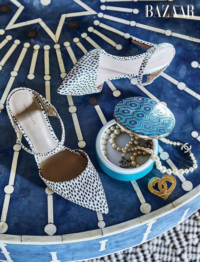 A pair of Ann Taylor heels, a trinket box filled with a Chanel necklace, and a brooch sit atop a coffee table from India.