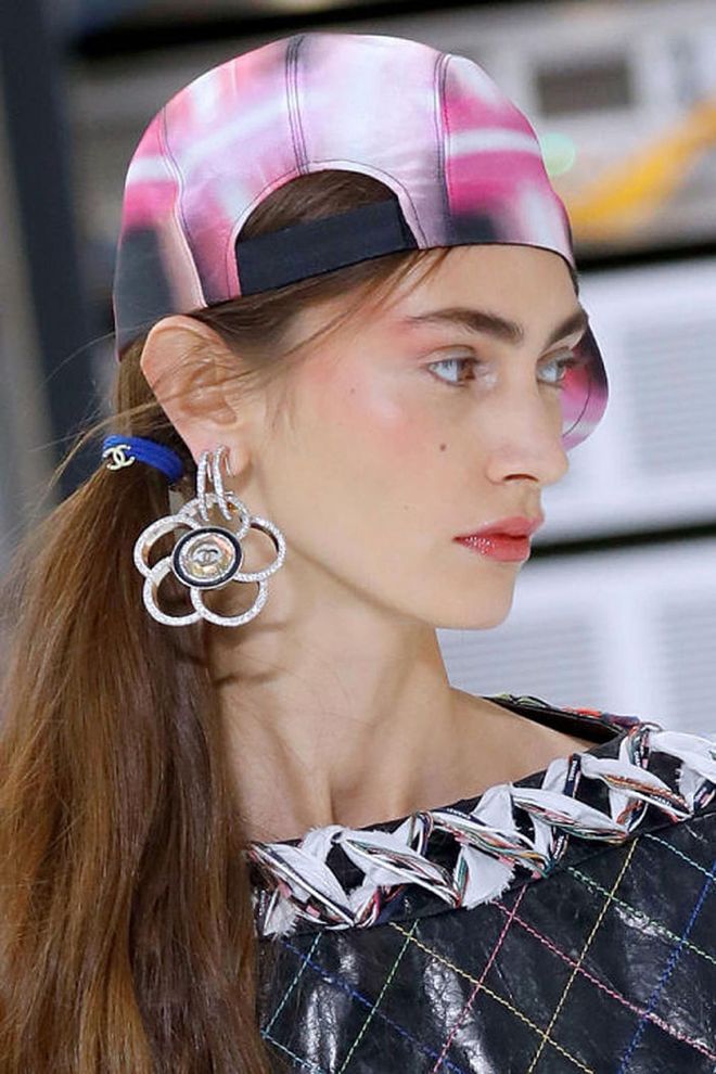 The Look: Back To The Future
How-To: The Chanel show this season was a look at a technological future through the lens of the colorful 1990s tech boom.This playful mix of technology of the past and future was clearly what inspired hairstylist Sam McKnight and makeup artist Tom Pecheux. The hair was fastened in a low side ponytail with a neon hair bauble covered in plastic Chanel charms. It looked exactly like something we would have worn in the early '90s except, you know, it was Chanel. The lips were covered in a bright pink glossy lipstick that matched a similar shade of blush traced across the cheekbones, up toward the temples, and to the eyes. It was a nod to draping, the heavy-handed blush technique popularized in the '80s and '90s. This isn't the first show we've seen reference draping this season (just look to Emporio Armani, Kenzo, or Adam Selman ). The bottom line? Get your blush brushes ready: you're going to need them in a big way come next spring.