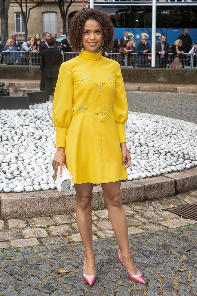 Gugu Mbatha-Raw in a yellow embroidered mini dress styled with satin pink court shoes.

Photo: Getty
