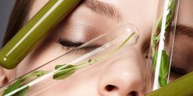 close up beauty shot of a female face that has test tubes filled with green smoothie and leafy plants in it- symbolizing organic make-up and natural beauty treatment