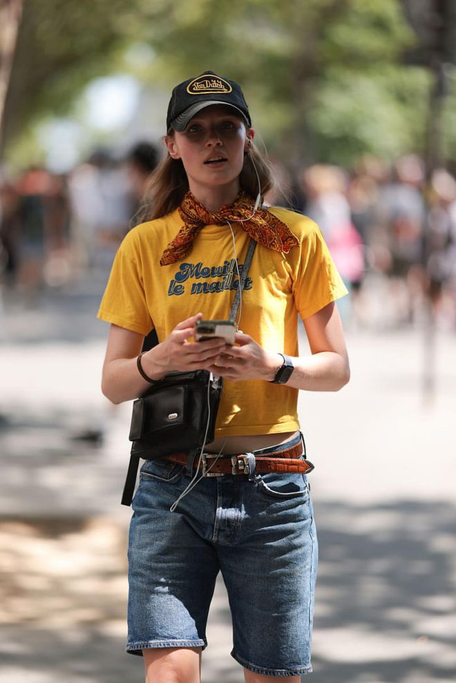 PARIS, FRANCE - JUNE 25: Fashion Week Guest is seen wearing  a black and yellow cap, a short jeans, a yellow tshirt, yellow and brown  scarf around her neck and a black leather bag outside during the Sacai Menswear Spring/Summer 2024 as part of  Paris Fashion Week on June 25, 2023 in Paris, France. (Photo by Jeremy Moeller/Getty Images)