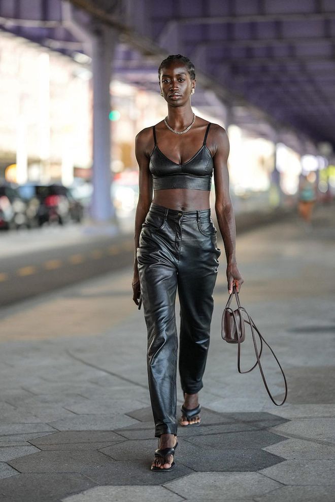 NEW YORK, NEW YORK - SEPTEMBER 10: A guest wears gold earrings, a gold large chain necklace, a black shiny leather V-neck / cropped tank-top, black shiny leather large pants, a dark brown shiny leather handbag from Telfar, black shiny puffy leather flip flop heels sandals , outside Jason Wu, during New York Fashion Week, on September 10, 2022 in New York City. (Photo by Edward Berthelot/Getty Images)