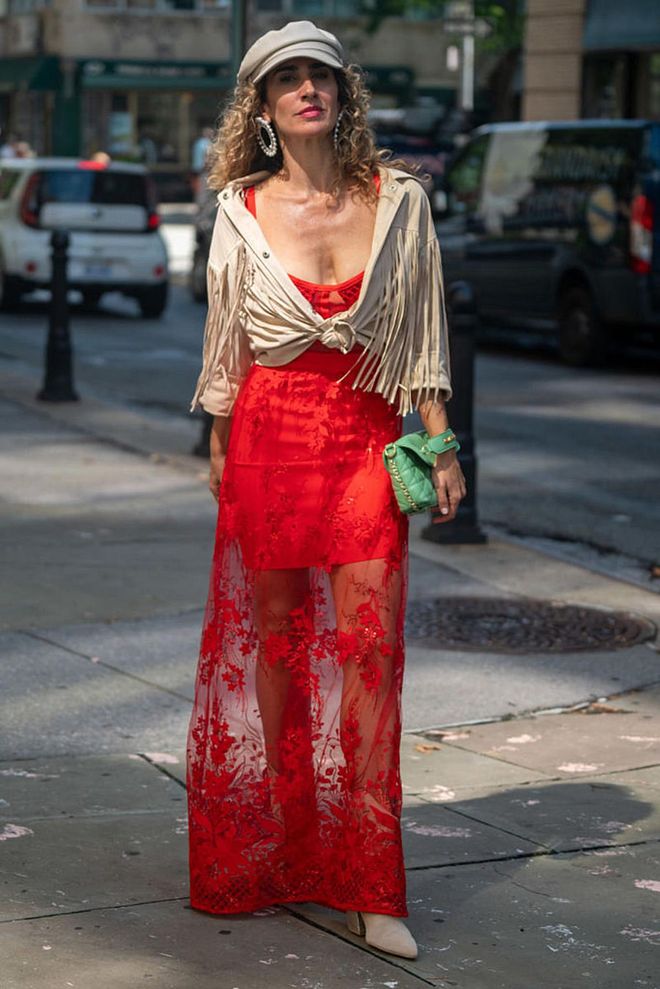 NEW YORK, NEW YORK - SEPTEMBER 13: Vanessa Calderon wearing a long red laced dress with a beige long sleeve outerwear with tassels, matched with a green clutch bag. (Photo by David Dee Delgado/Getty Images)