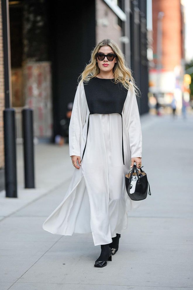 NEW YORK, NEW YORK - SEPTEMBER 10: A guest wears black sunglasses, a black breastplate, a white long sleeves long oversized shirt dress, a black shiny leather handbag from Jil Sander, black shiny leather block heels shoes from Prada, gold rings, outside Tibi , during New York Fashion Week, on September 10, 2022 in New York City. (Photo by Edward Berthelot/Getty Images)