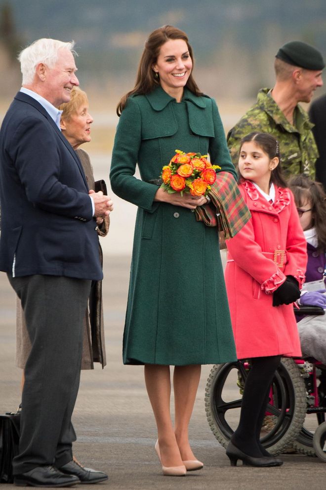 The Duchess wore a forest green Hobbs coat with a black leather belt at the waist, nude pumps and a plaid scarf at the Whitehorse airport. Photo: Getty