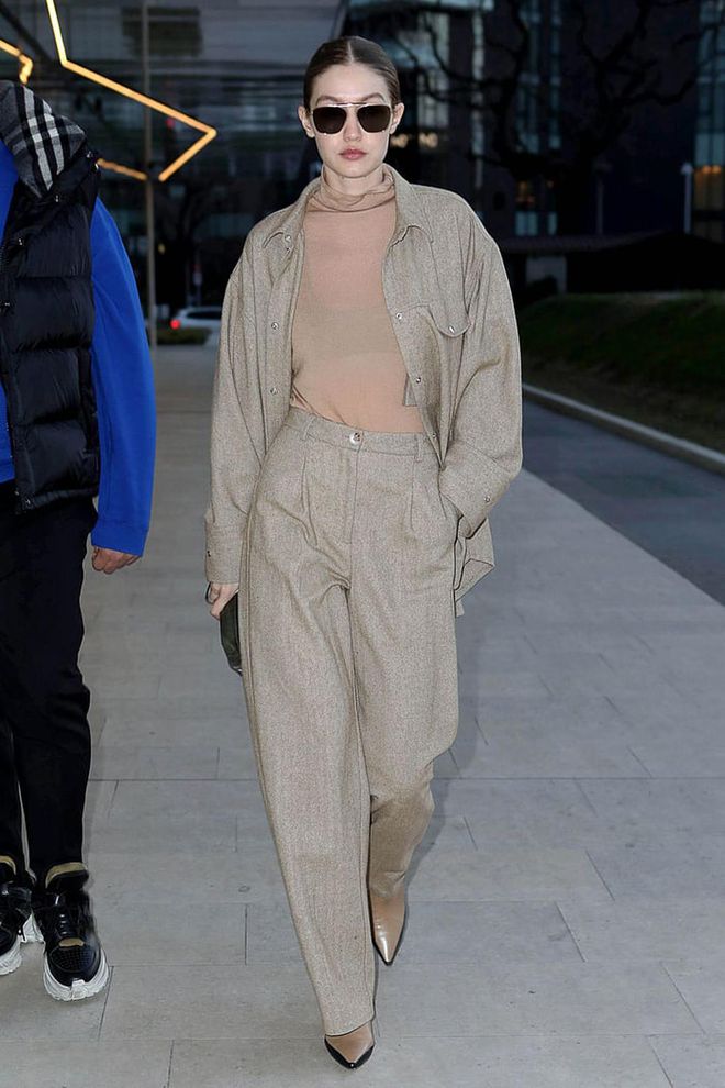In a sheer, nude turtleneck, matching neutral button-up and trousers, pointed nude boots by Wandler, and black shades.