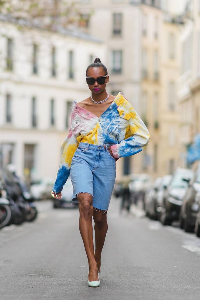 PARIS, FRANCE - MAY 21: Emilie Joseph @in_fashionwetrust wears diamond earrings, a silver chain necklace, black sunglasses, a white yellow blue and orange tie and dye denim jacket by Levis, a blue faded denim jean dad shorts by Mango, pointy pumps/ heels/ stilettos in pastel leather Jimmy Choo shoes, on May 21, 2021 in Paris, France. (Photo by Edward Berthelot/Getty Images)