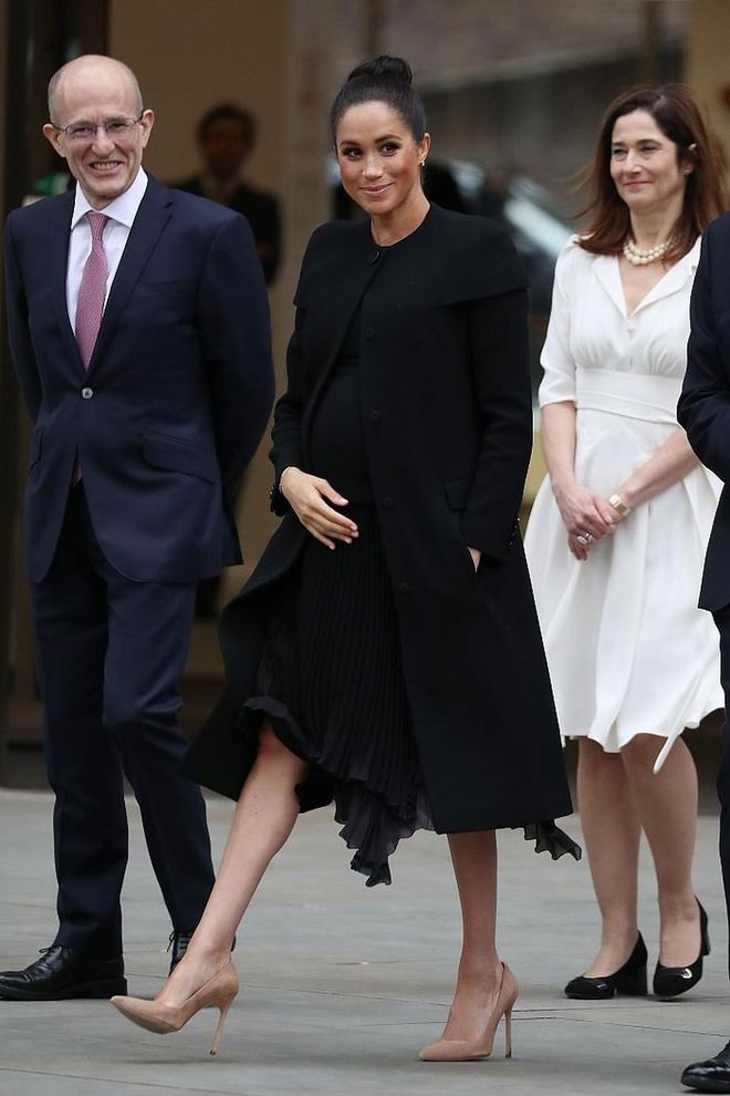 From beige to black, yet still a master of the monotone look. Meghan stepped out wearing head-to-toe Givenchy by Clare Waight Keller, featuring a custom coat with an interesting caplet detailing over a flowy black dress. She kept the rest of the look simple with just a pair of nude Manolo pumps and her hair worn in a sleek top knot. 