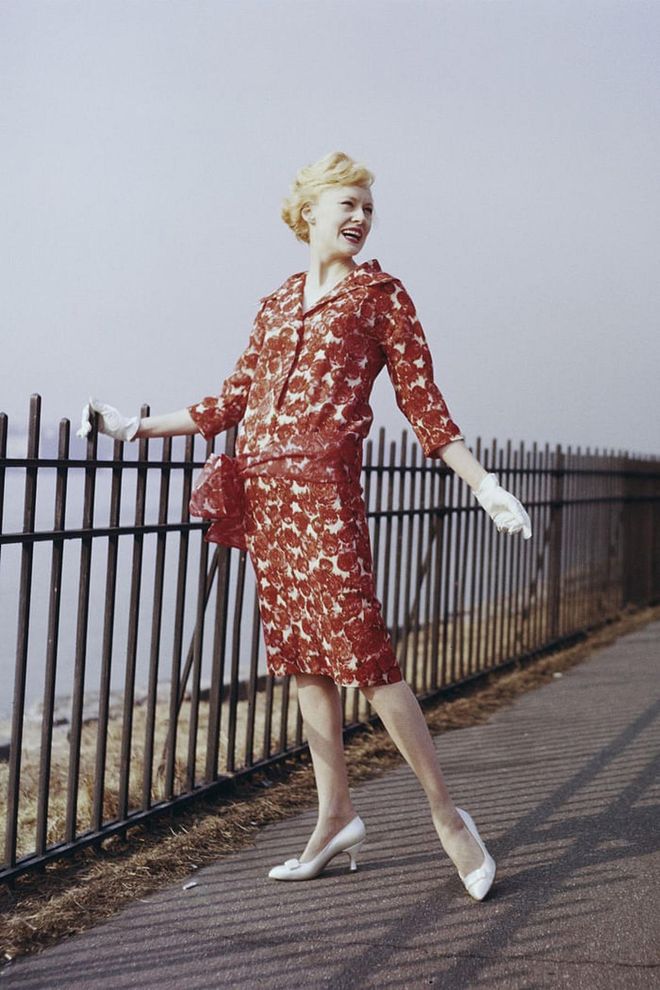 A woman posing in a red print dress, white gloves and pumps. Photo: Getty 