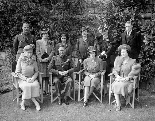 The royals pose for a family portrait outdoors. Queen Mary, King George VI, Princess Elizabeth, and Elizabeth the Queen Mother are seated in the front row, while the Duke and Duchess of Gloucester, Princess Margaret, Princess Mary the Countess of Harewood, the Duchess of Kent, and Henry Lascelles, 6th Earl of Harewood stand behind them.