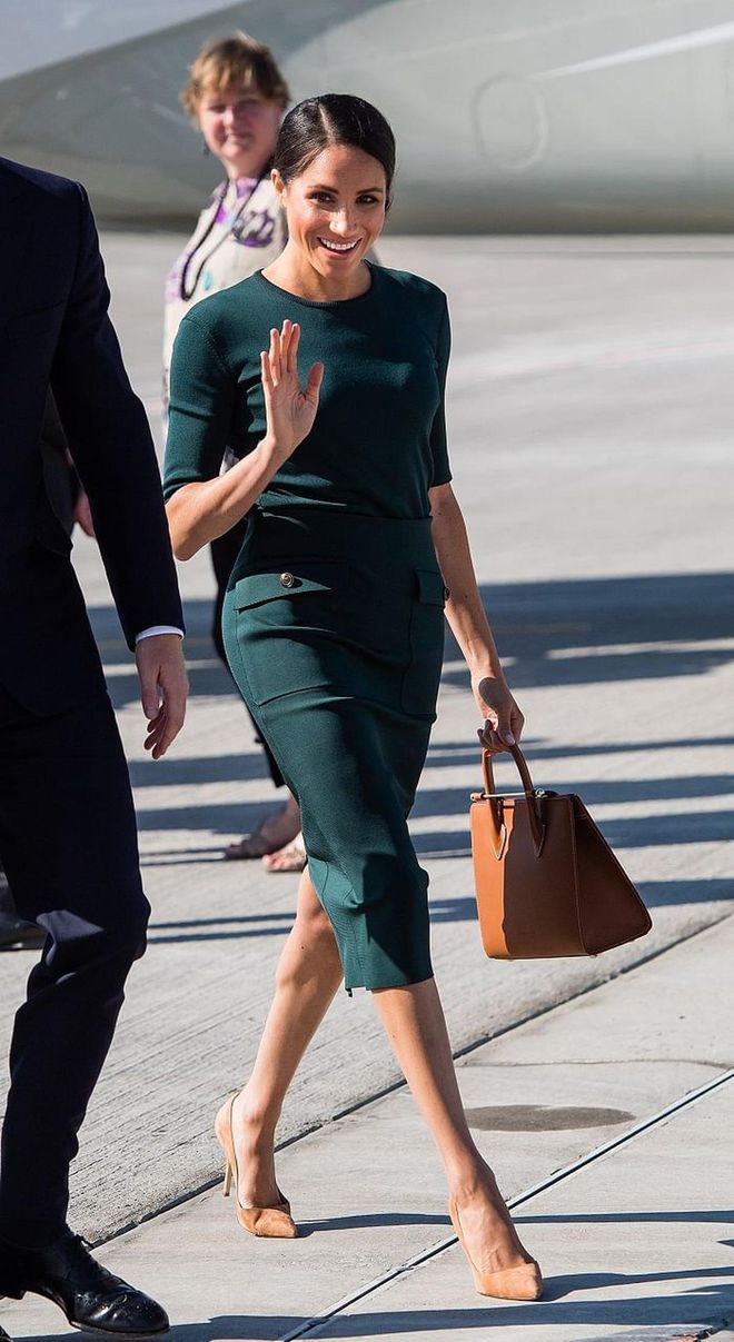 Duchess of Sussex arrives at Dublin Airport top-to-toe in Givenchy featuring a forest green pencil skirt and a matching green crew neck top. She accessorizes with a tan Strathberry Midi and nude pumps. 