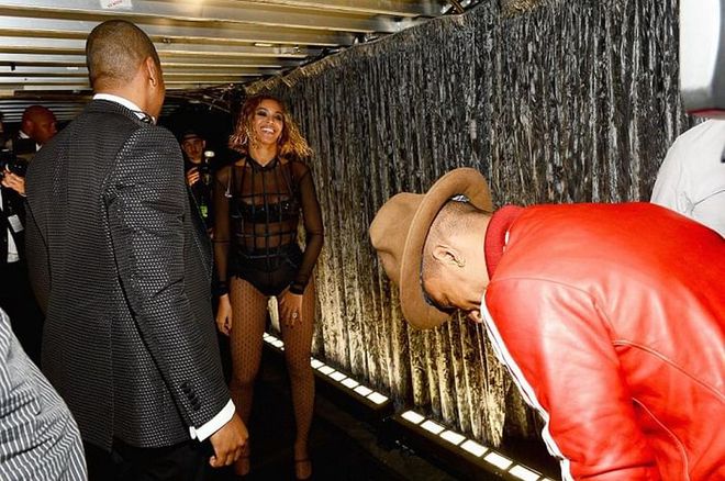 Beyoncé, wearing a structured black onesie, shares a laugh backstage with Jay Z and Pharrell Williams at the 56th Annual Grammy Awards. 