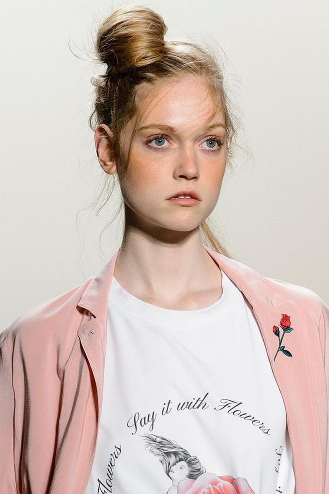 Off-kilter, wispy topknots are paired with a prominent nude peach blush at Adam Selman. Everything else is parred down to create "young, windswept girls." Photo: Getty