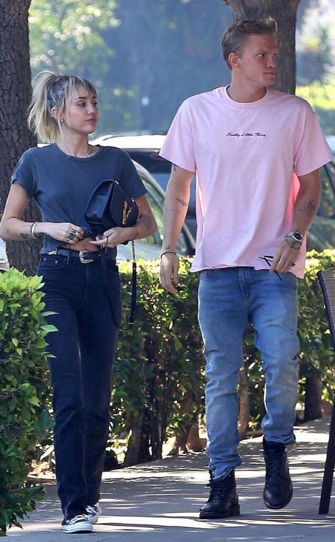 Miley out in Los Angeles with Cody Simpson dressed in black boot cut jeans, a faded grey shirt, Converse Chuck Taylors and a Versace leather top handle bag. 

Photo: Courtesy
