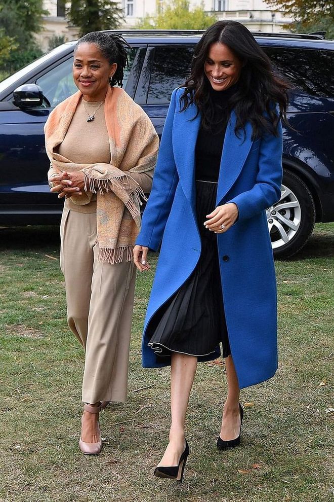 Meghan kept with the theme of vibrant blue when she showed up for her cookbook launch in a zephyr blue Smythe coat over a turtleneck and black pleated skirt by Misha Nonoo. 