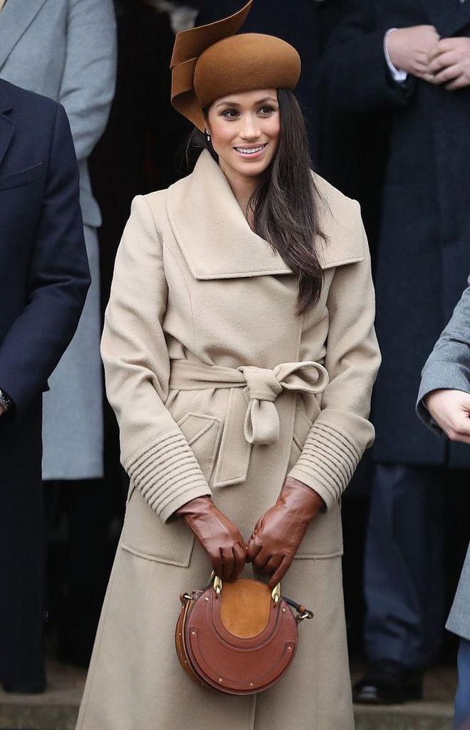 Meghan celebrated Christmas with the British Royal Family in an understated camel wrap coat from Sentaler. She was all about the browns, accessorizing with a Chloe Pixie Round Bag in tan, Stuart Weitzman Highland Boots in nutmeg suede and even brown gloves to match. The beret hat was a royal must-have by Philip Treacy. 