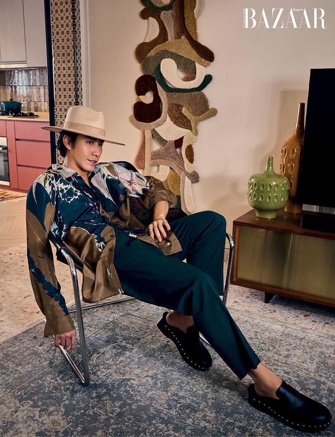 Sitting in front of a tapestry by Mira Sohlén in his living room, Hong wears a Dries Van Noten top, Kind trousers, Hermès clogs, and a hat from Born In Colour.