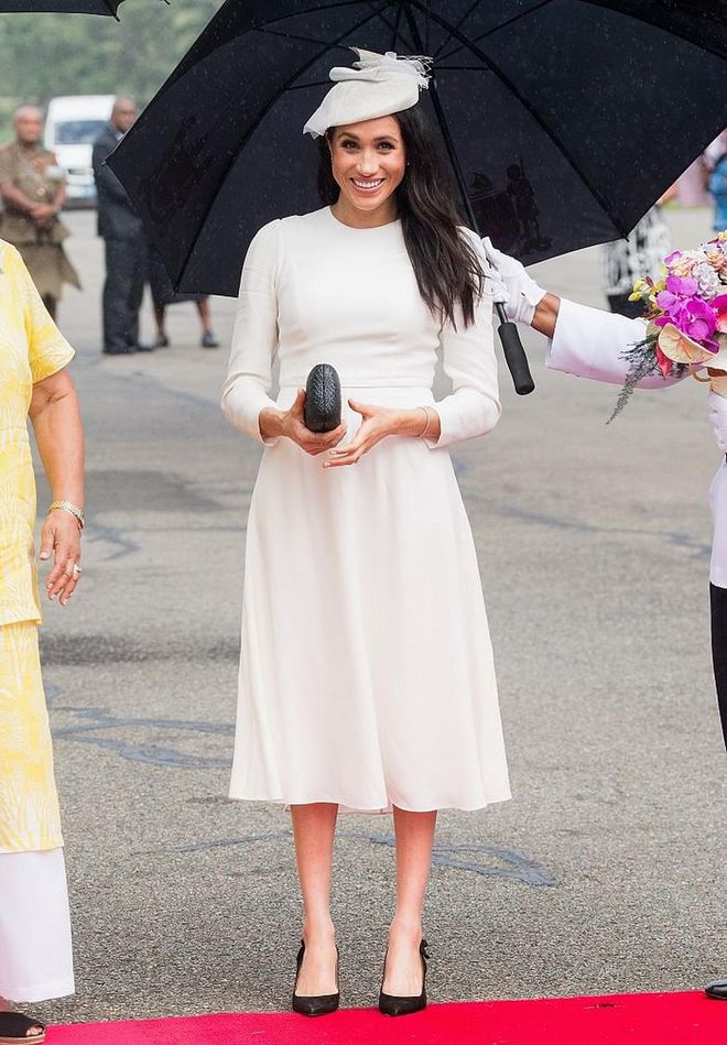 The Duchess of Sussex touched down in Fiji wearing a custom white Zimmermann dress and a matching white Stephen Jones fascinator. She carried a black straw clutch by Kayu. 